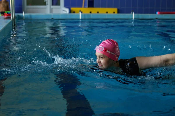 Woman swims in swimming pool. Goggles and swimming cap. Concept of sports, exercise and healthy lifestyle