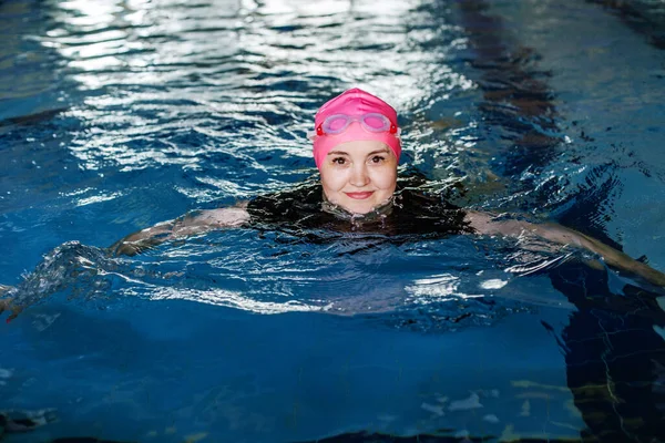 Woman swims in swimming pool. Goggles and swimming cap. Concept of sports, exercise and healthy lifestyle
