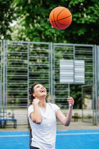 Concept of sports, hobbies and healthy lifestyle. Young athletic woman is training to play basketball on modern outdoor basketball court.