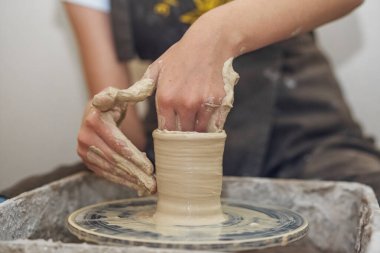 Potter girl works on potter's wheel, making ceramic pot out of clay in pottery workshop. Art and hobby concept
