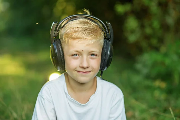 Preteen boy listening to song or audio book. Blond boy uses headphones. Concept of music, radio and songs, technology