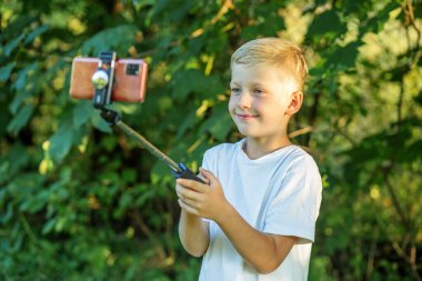 Child boy communicates via video chat, uses smart phone, tripod and Internet. Concept of technology and blogging.