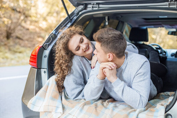Boy and girl are hugging in trunk of car. Autumn forest. Couple in love. Romantic date. Concept for love, happy family, travel and weekend