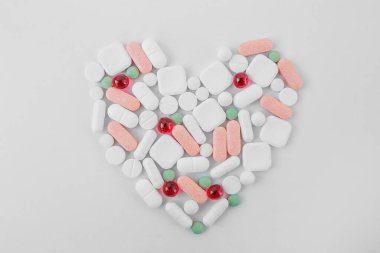 Many different pills on white background, laid out in form of heart. Copy space. Top view. Concept of pharmaceuticals, medicine and healthcare
