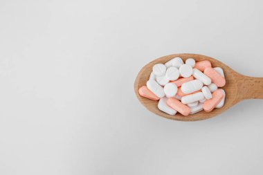 Many different pills in wooden spoon on white background. Copy space. Top view. Concept of pharmaceuticals, medicine and healthcare