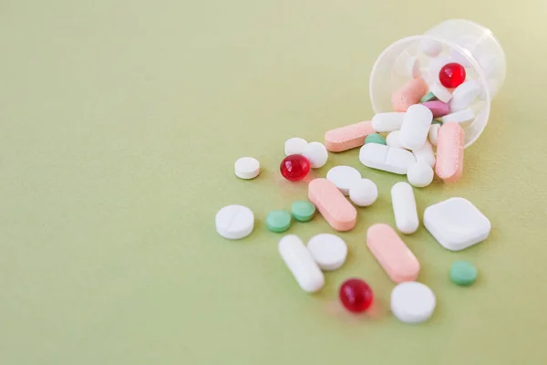 Many different pills in plastic cup on green background. Copy space. Concept of pharmaceuticals, medicine and healthcare