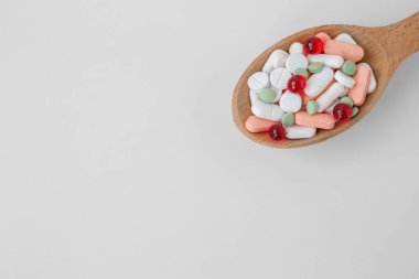 Many different pills in wooden spoon on white background. Copy space. Top view. Concept of pharmaceuticals, medicine and healthcare