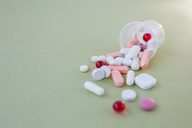 Many different pills in plastic cup on green background. Copy space. Concept of pharmaceuticals, medicine and healthcare