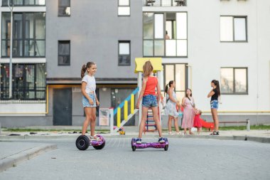 Aktif yaşam konsepti. Yazın uçan kaykaylara binen mutlu çocuklar ya da dışarıda gezen scooterlar. Çok katlı binanın yanındaki oyun parkı.