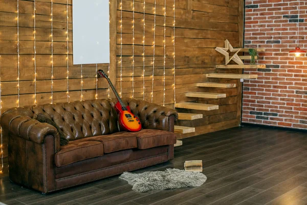 Loft style room interior with leather sofa and wooden wall. Electric guitar and book in room