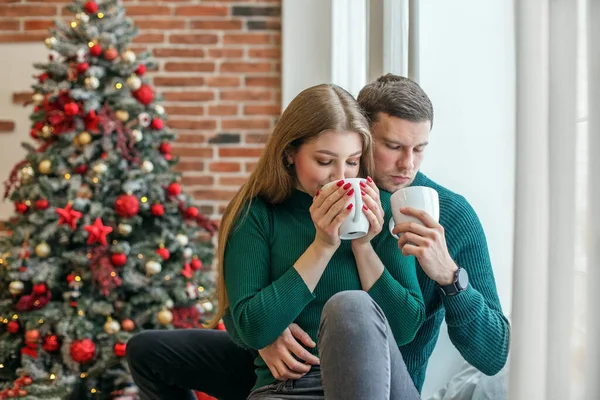 Couple hugs and drinks hot coffee near window. Concept of family, Christmas and winter season.