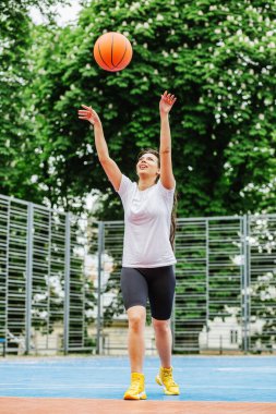 Spor anlayışı, hobiler ve sağlıklı yaşam tarzı. Genç atletik kadın, modern açık hava basketbol sahasında basketbol oynamak için antrenman yapıyor..