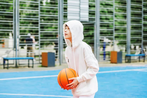 Concept of sports, hobbies and healthy lifestyle. Child schoolboy trains playing basketball on summer day.