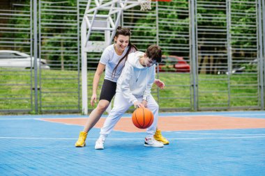 Kız ve küçük kardeşi, genç kız, açık gökyüzünün altında, modern basketbol sahasında basketbol oynuyorlar. Spor anlayışı, hobiler ve sağlıklı yaşam tarzı.
