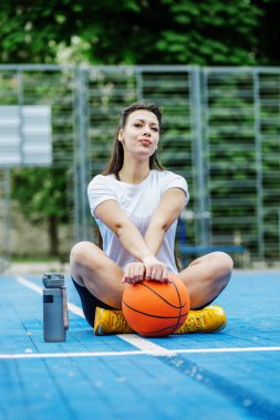Yeniden kullanılabilir su şişesi. Bayan sporcu basketbol sahasında dinleniyor, su içiyor. Spor ve hobi kavramı.