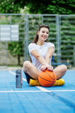 Yeniden kullanılabilir su şişesi. Bayan sporcu basketbol sahasında dinleniyor, su içiyor. Spor ve hobi kavramı.