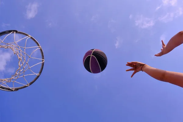 Street basketball ball player throwing ball into the hoop. Close up of hands, black and violet ball near the hoop with blue sky in the background