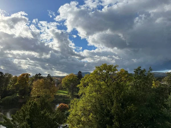 Mavi ve güneşli bulutlu gökyüzü ile tepedeki ağaçlar