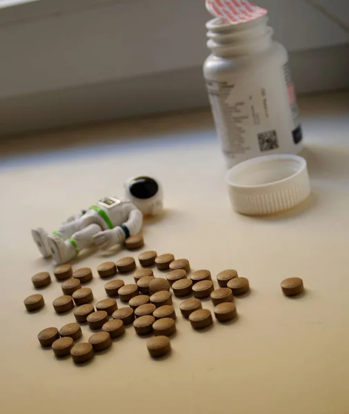 a toy astronaut in a white spacesuit lies against the background of vitamins and a jar for vitamins