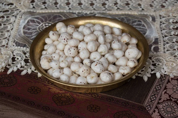 Crispy Lotus pops Seeds or Phool Makhana or Fox Nuts popular dry snacks from India served in a brass plate. Side view. Makhana from Mithila region of Bihar in India. Mithilanchal. selective focus