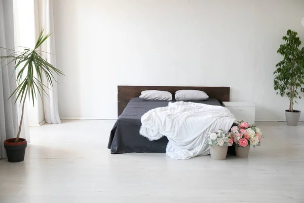Interior de un dormitorio blanco con una cama y plantas con flores — Foto de Stock