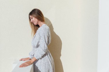 Beyaz elbiseli güzel bir kadın balkonda dikilip dışarıya bakıyor.