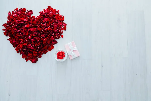 Regalo de pétalos de rosa roja en forma de corazón sobre un fondo claro — Foto de Stock