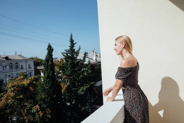 Piękna blondynka kobieta w szarej sukience wygląda z balkonu — Zdjęcie stockowe