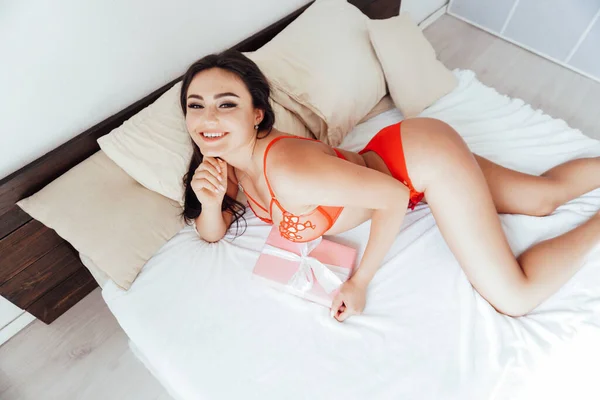 Schöne Brünette in roten Dessous wachte morgens im Bett im Schlafzimmer auf — Stockfoto