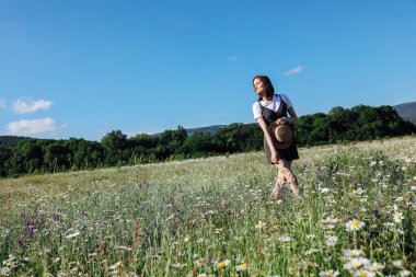 Tarlada papatyalarla yürüyen elbiseli bir kadın.