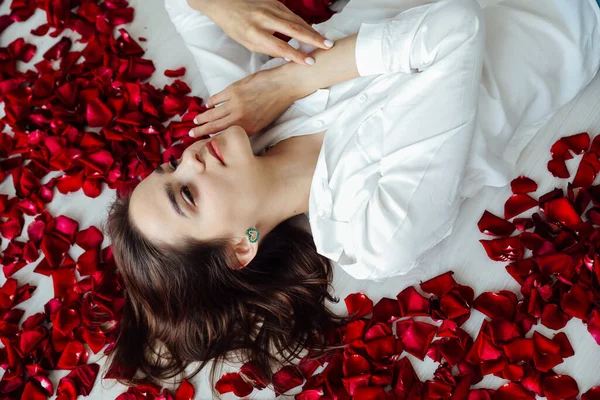 Gyönyörű nő fekszik a szirmok egy vörös rózsa — Stock Fotó