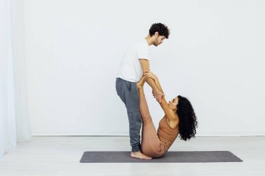 Bir kadın ve bir erkek, beyaz bir odada çift yoga yapıyorlar.