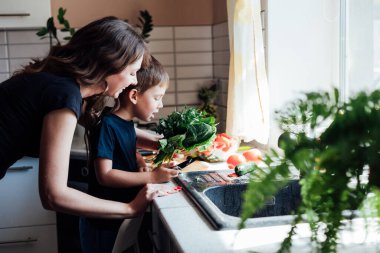 Anne ve oğlu mutfakta öğle yemeğinde salata için taze sebze hazırlıyorlar.
