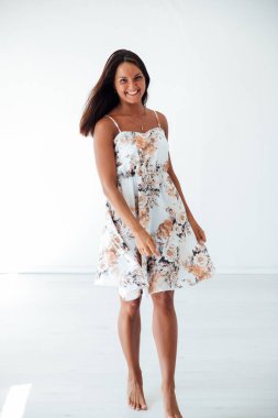 Beyaz bir odada, yazlık elbiseli esmer bir kadın.