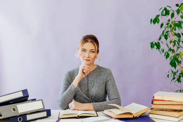 Una mujer de negocios en un traje se sienta en un escritorio de oficina con libros — Foto de Stock