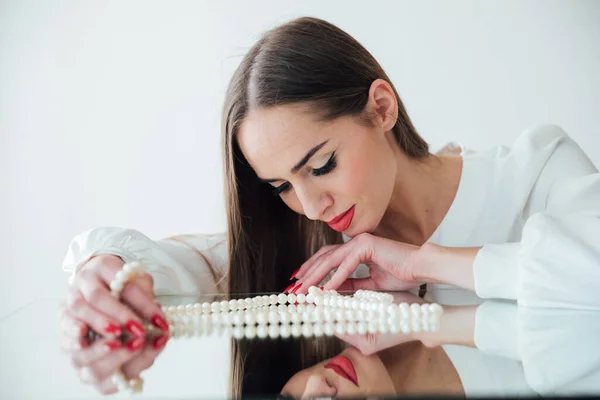 Porträt einer schönen brünetten Frau am Spiegel mit Perlen — Stockfoto