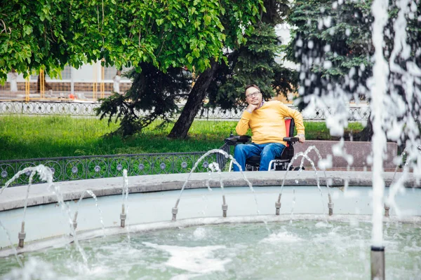 Um homem com deficiência em uma cadeira de rodas caminha pela cidade — Fotografia de Stock