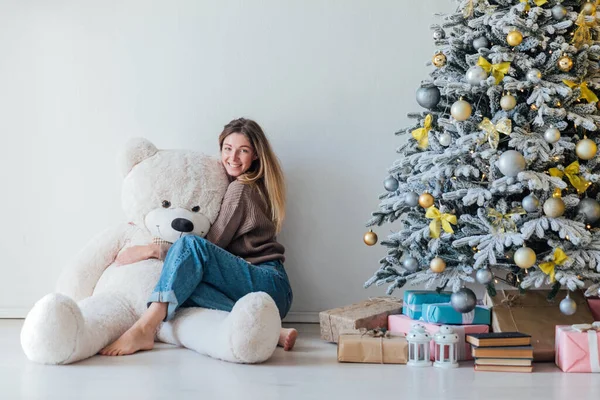 Güzel bir kadın oyuncak ayıyla beyaz bir Noel ağacında yeni yıl hediyeleriyle