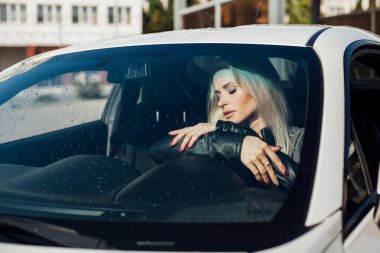 Güzel sarışın kadın beyaz bir araba kullanıyor.