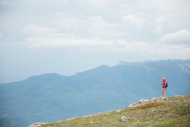 Dişi gezgin bir dağın tepesinde durmuş manzaraya bakıyor.
