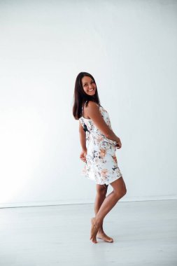 Güzel, bronzlaşmış bir kadın, beyaz bir odada çiçekli bir yaz elbisesi içinde.