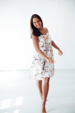 Güzel, bronzlaşmış bir kadın, beyaz bir odada çiçekli bir yaz elbisesi içinde.