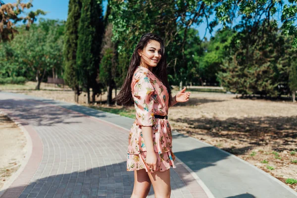 Krásná brunetka žena v šatech s květinami procházky po ulici a parku — Stock fotografie