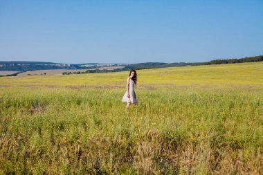 Yazlık elbiseli güzel bir kadın tarlada yürüyor.