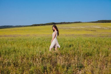 Yazlık elbiseli güzel bir kadın tarlada yürüyor.