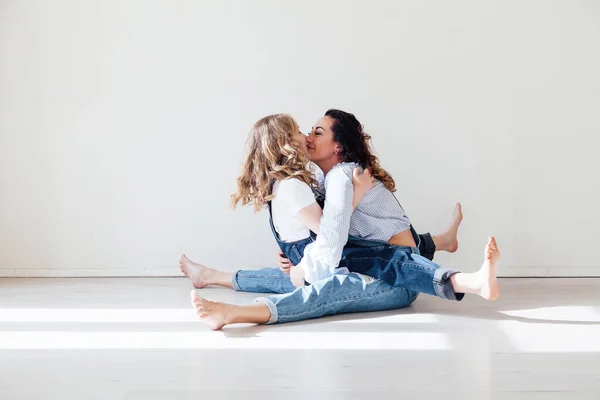 Madre e hija en jeans se sientan abrazando y sonriendo — Foto de Stock