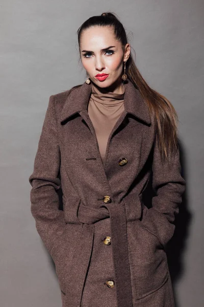 Vrouw in een warme bruine jas op een grijze achtergrond — Stockfoto