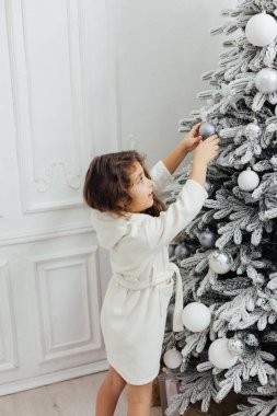 Küçük kıvırcık kız Noel ağacını hediyelerle süslüyor.