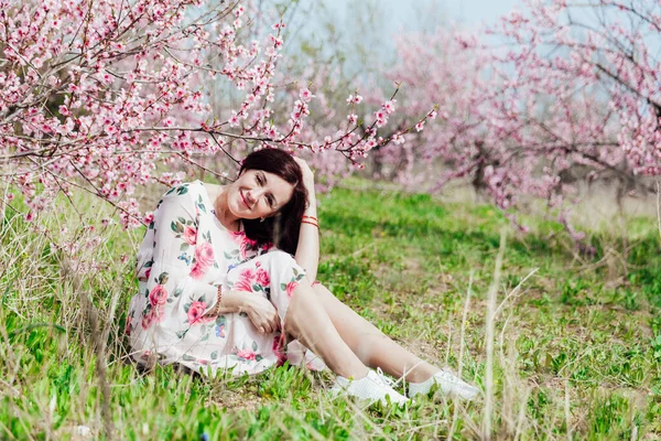 Hermosa mujer en un vestido de primavera en un jardín floreciente con hierba verde —  Fotos de Stock