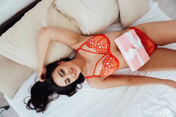 Schöne brünette Frau in rotem Leinen auf dem Bett im Schlafzimmer — Stockfoto